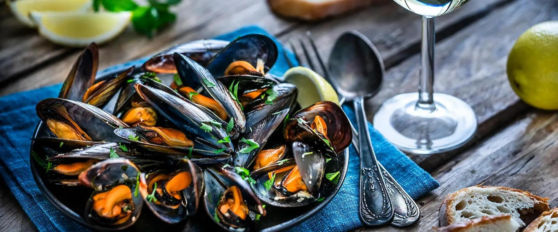 Cozze succulente con prezzemolo, limone e vino bianco su tavola rustica.