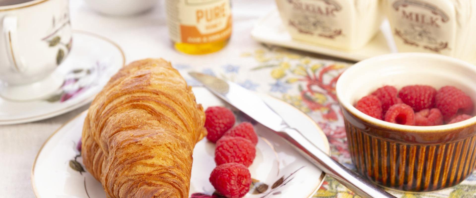 Colazione elegante: croissant dorato, lamponi freschi, tazza di tè su tovaglia floreale.