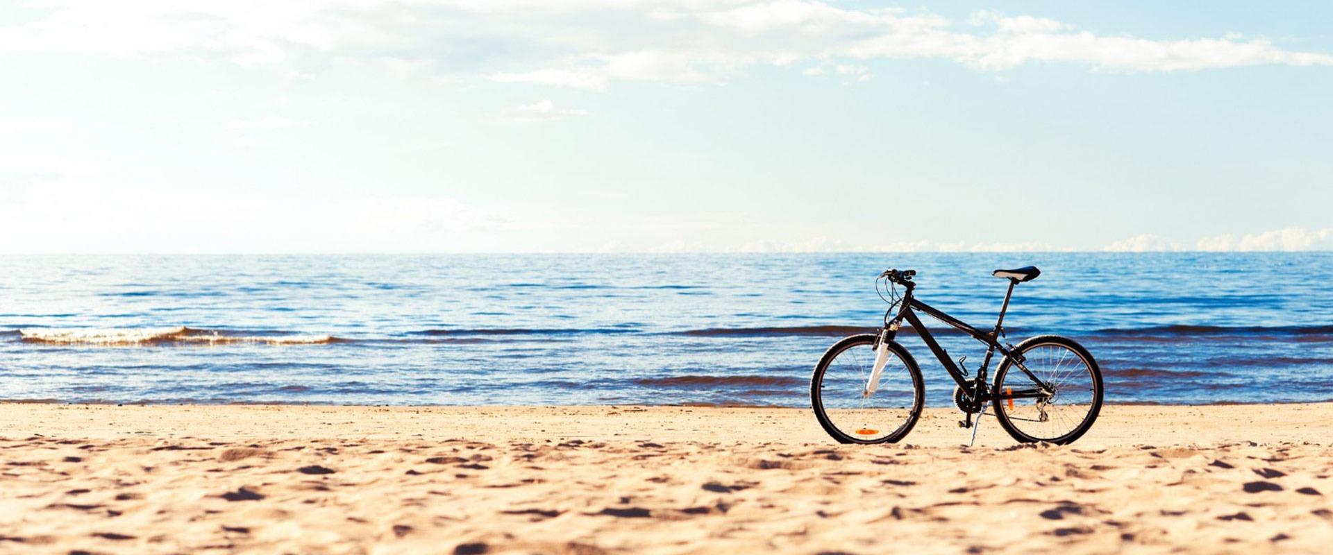 Bicicletta solitaria su spiaggia assolata, onde calme e cielo azzurro evocano serenità.