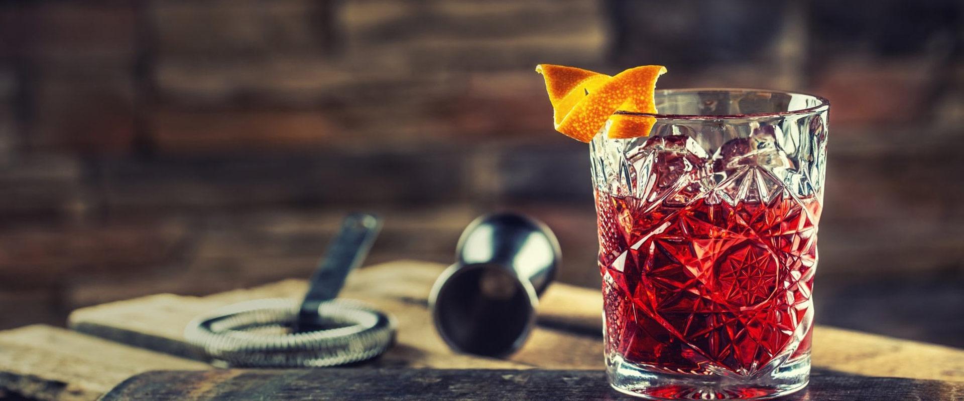Bicchiere di cristallo con cocktail rosso, guarnito con scorza d'arancia, su tavolo rustico.
