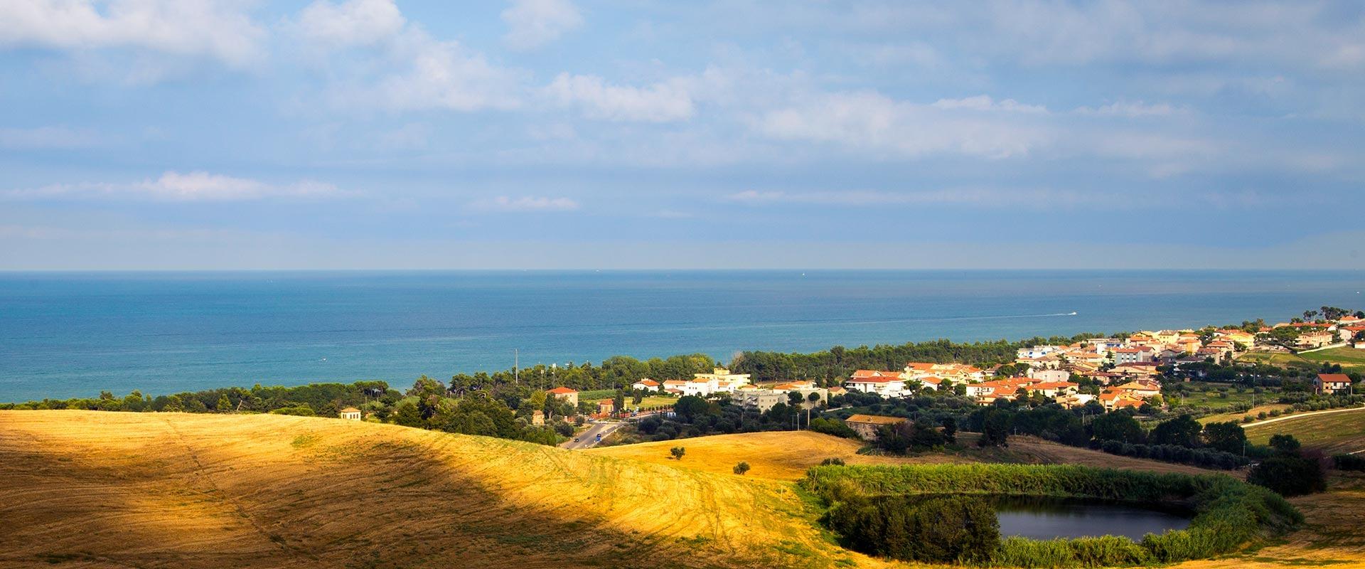 Paesaggio marino con campi dorati, cielo azzurro e un tranquillo villaggio costiero.