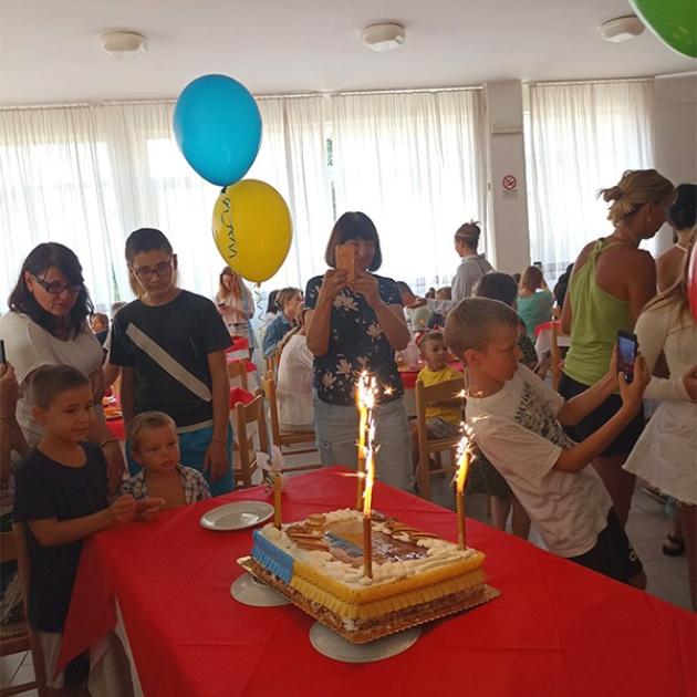 Festa di compleanno gioiosa con bambini, torta colorata e scintille, palloncini blu e gialli.