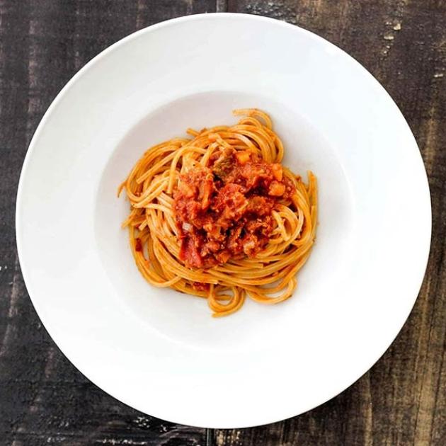 Spaghetti al sugo rosso, serviti con eleganza su un piatto bianco, atmosfera rustica.