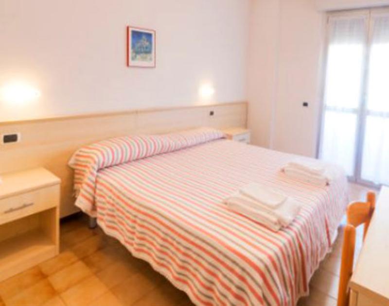 Camera luminosa con letto matrimoniale, copriletto a righe colorate, atmosfera accogliente e rilassante.