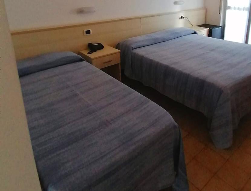 Camera semplice, due letti matrimoniali, copriletti blu, atmosfera accogliente e tranquilla.